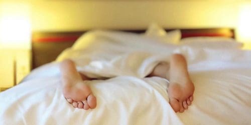 A person relaxing on a bed with feet under white sheets, conveying serenity.